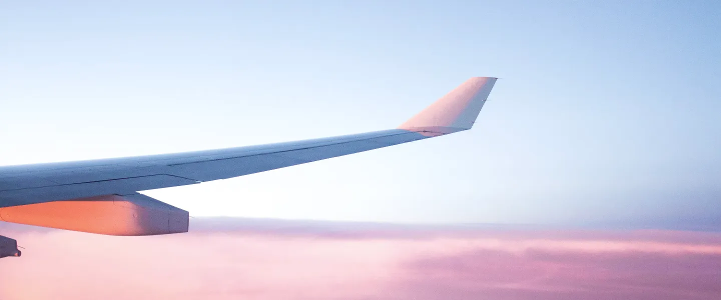 Airplane wing above pink sunset clouds